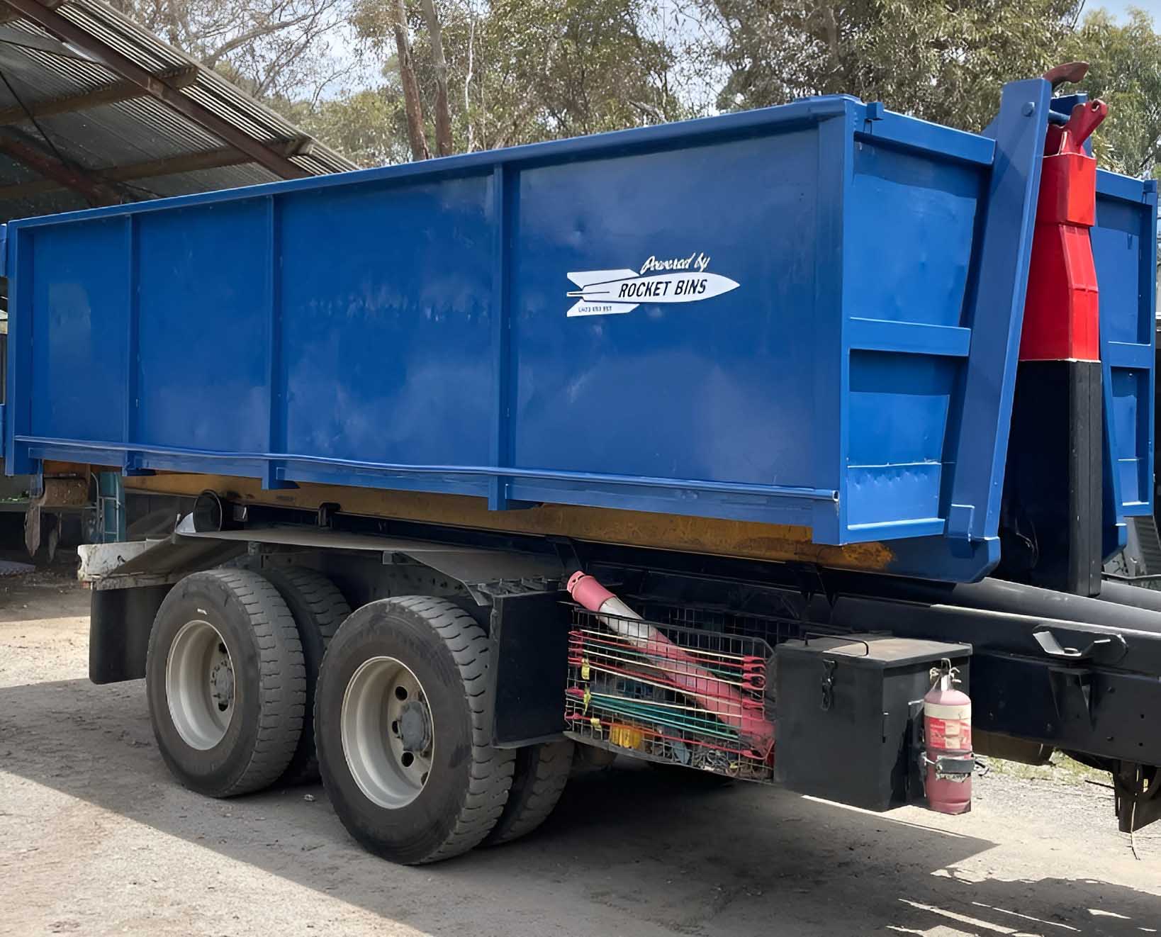1-mobile Blue hook-lift bin loaded on the back of a truck under a shed