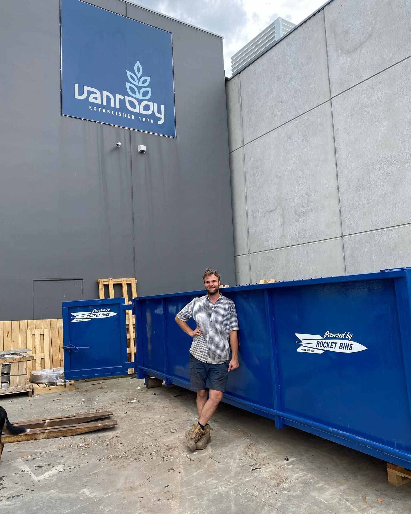 about Man standing beside a long blue walk-in bin with its door open outside a commercial building