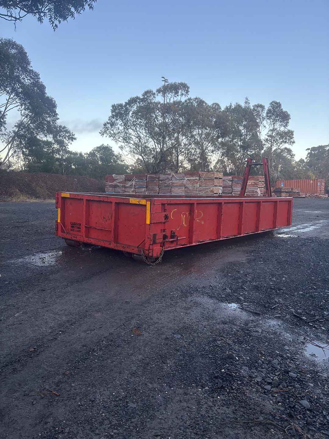 s1b Red 6m³ walk-in bin in a yard with pallets of bricks behind