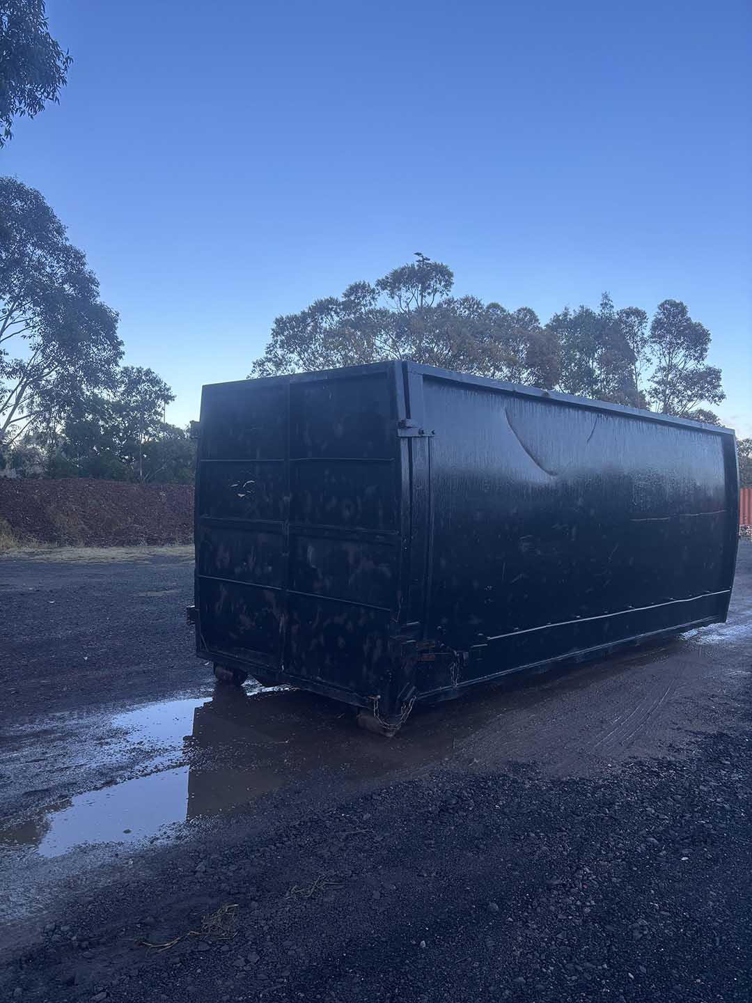 s7b Black 30m³ walk-in bin in a wet yard, doors closed